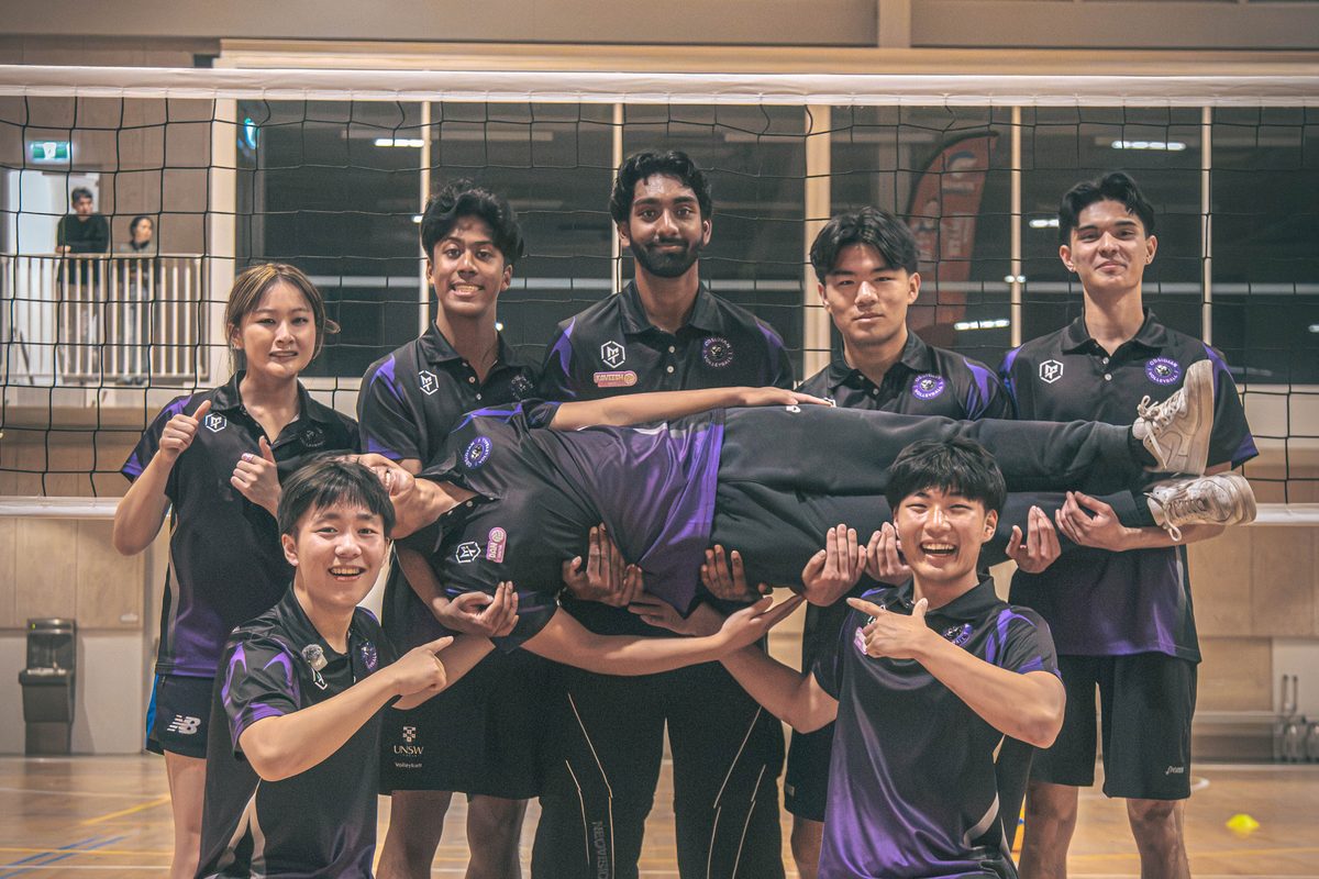 Obsidian coaching team in purple polos laughing together while lifting a coach horizontally on court